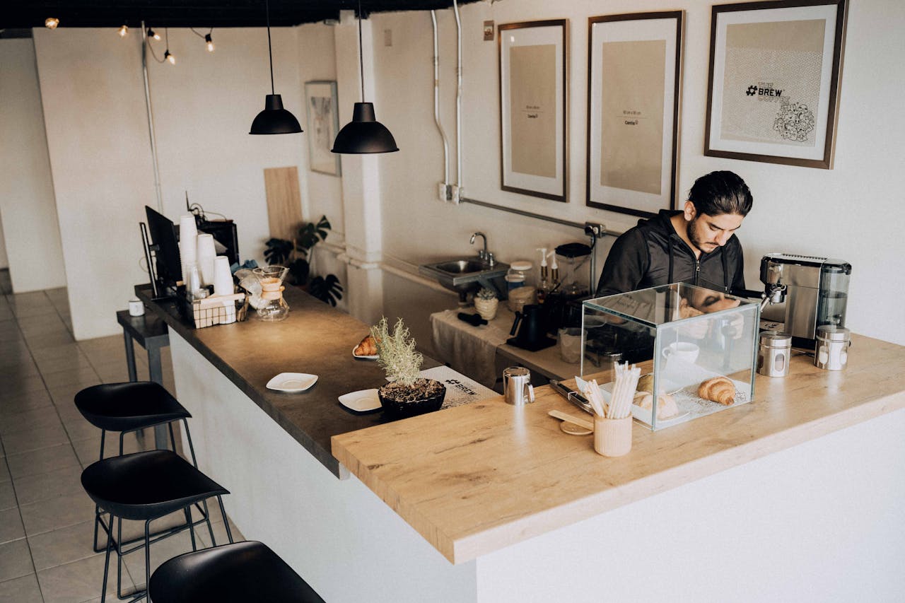 hero-img A barista works in a modern café with minimalistic décor and warm lighting.